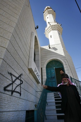 A Palestinian man wearing the traditional head scarf points on December 2, 2008 at graffitti sprayed at the entrance of the mosque in the West Bank village of Sinjel, near Ramallah, by a group of Israeli settlers earlier in the day. The graffiti in Hebrew reads 