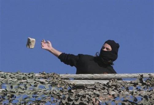 A Jewish settler throws a stone from a rooftop overlooking Palestinian houses in the West Bank city of Hebron, Tuesday, Dec. 2, 2008. Dozens of Jewish settlers rioted Tuesday in the West Bank town of Hebron, clashing with the Israeli troops who guard them but who may also soon evict them from a disputed building they
