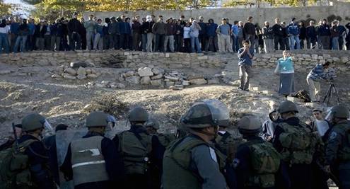 Israeli border policeman stand guard opposite Jewish settlers near a disputed house in the flashpoint West Bank city of Hebron on December 3, 2008. Israeli settlers and supporters prepared to battle a forceful eviction today after Israel declared a closed military area around the house, occupied in defiance of a court order. The settlers insist they have not only a God-given right to all of the biblical land of Israel, but that they are also legally in the house that a Jewish-American businessman claims he bought so more Jews can live in Hebron. The original Palestinian owner denies selling it, and the High Court has ordered the settlers out until ownership can be determined. From Getty Images by AFP/Getty Images.