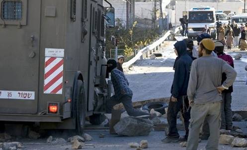 Jewish settlers stand next to an Israeli military vehicle during clashes with border policemen (not seen) outside a disputed house in the flashpoint West Bank city of Hebron December 3, 2008. Israeli settlers and supporters prepared to battle a forceful eviction today after Israel declared a closed military area around the house, occupied in defiance of a court order. The settlers insist they have not only a God-given right to all of the biblical land of Israel, but that they are also legally in the house that a Jewish-American businessman claims he bought so more Jews can live in Hebron. The original Palestinian owner denies selling it, and the High Court has ordered the settlers out until ownership can be determined. From Getty Images by AFP/Getty Images.